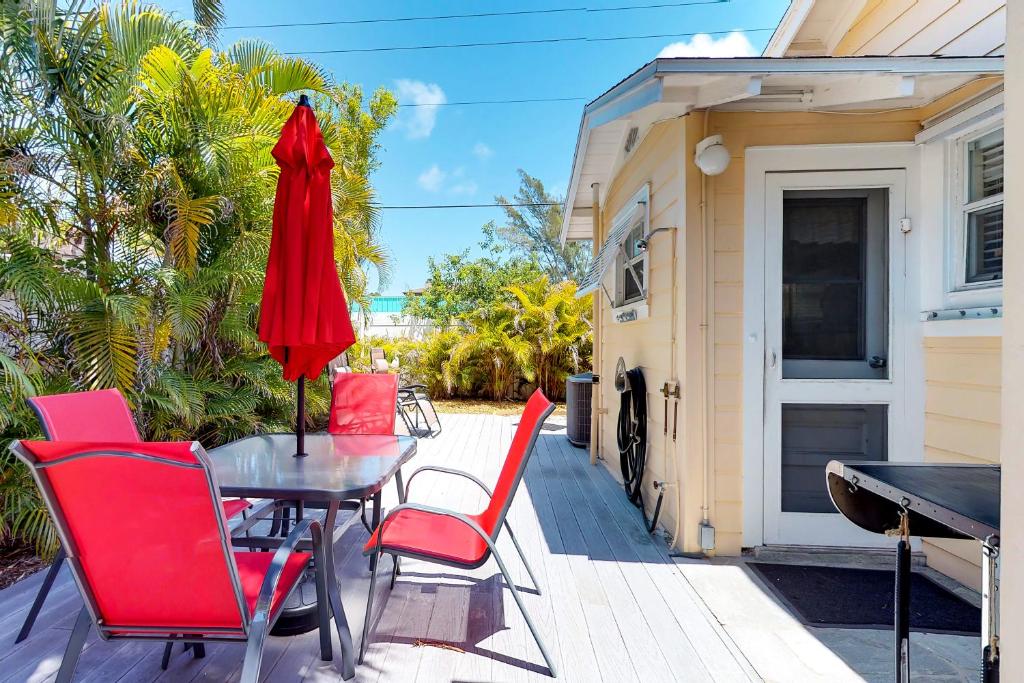 a patio with red chairs and a table with a red umbrella at The Seashell Cottage in Anna Maria