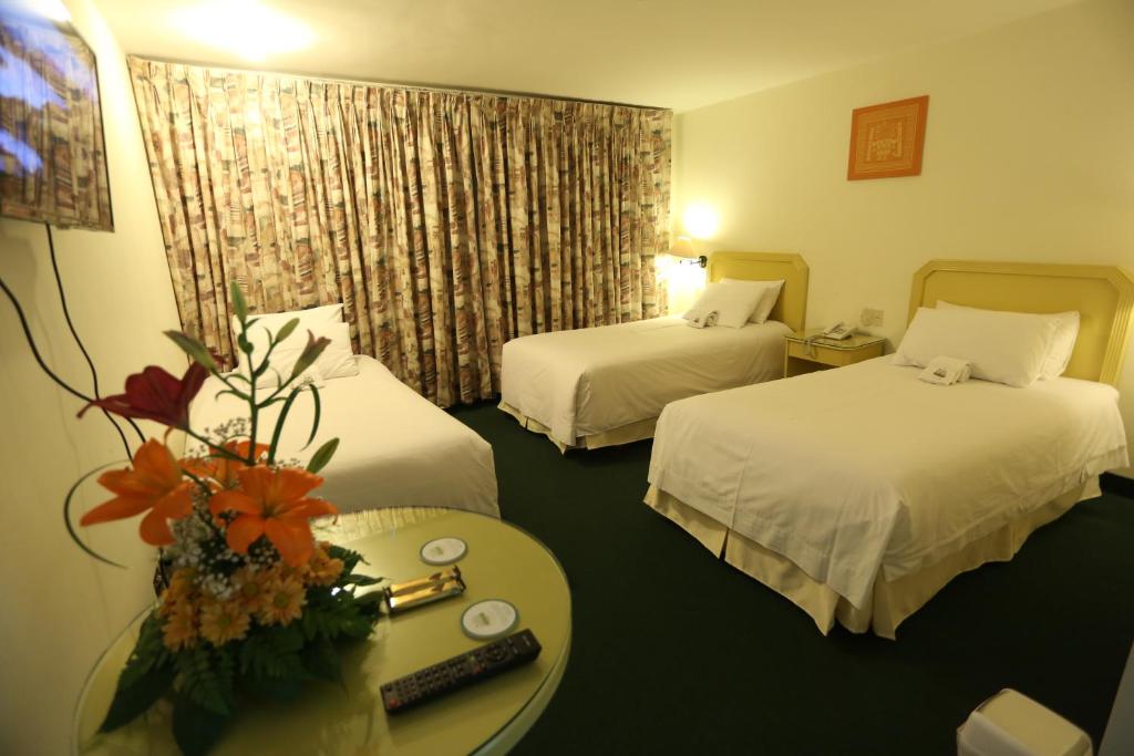 a hotel room with two beds and a table with flowers at Plaza Mayor Hotel in Puno