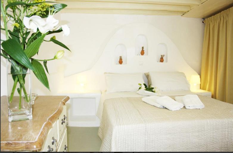ein weißes Schlafzimmer mit einem Bett und einer Vase aus Blumen in der Unterkunft Mariakis Luxury Studios in Astypalea-Stadt