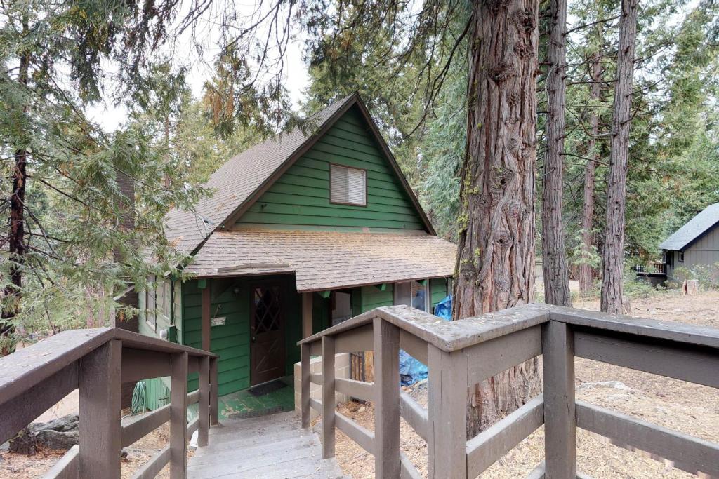 una casa verde con un puente de madera en el bosque en Blue Meadow Cottage en Shaver Lake