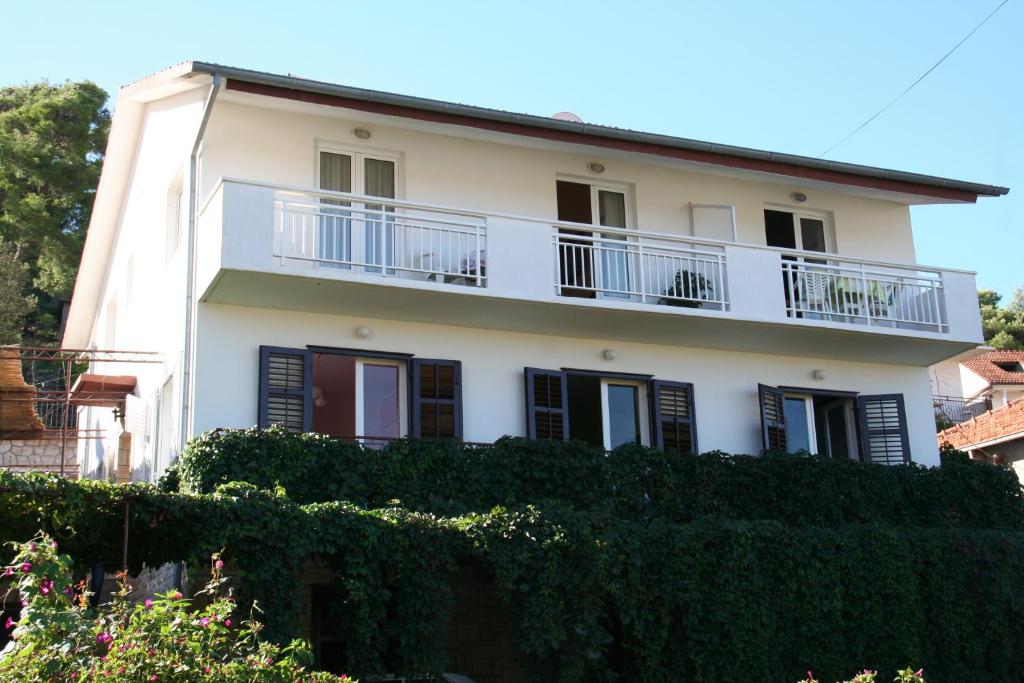 a white house with a balcony and bushes at Apartments Goic in Jelsa