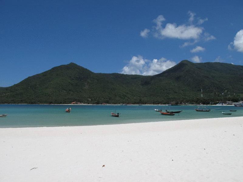 a group of boats on a beach with mountains in the background at Malibu Beach Bungalows in Chaloklum