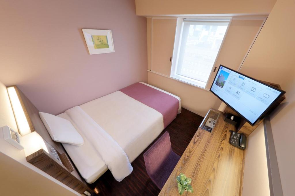 a small room with a bed and a computer monitor at Keio Presso Inn Ikebukuro in Tokyo