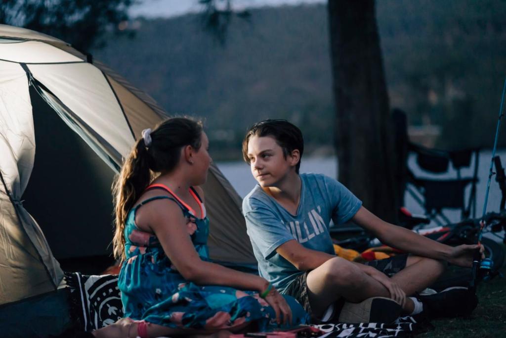 Un uomo e una donna seduti accanto a una tenda di Del Rio Riverside Resort a Wisemans Ferry