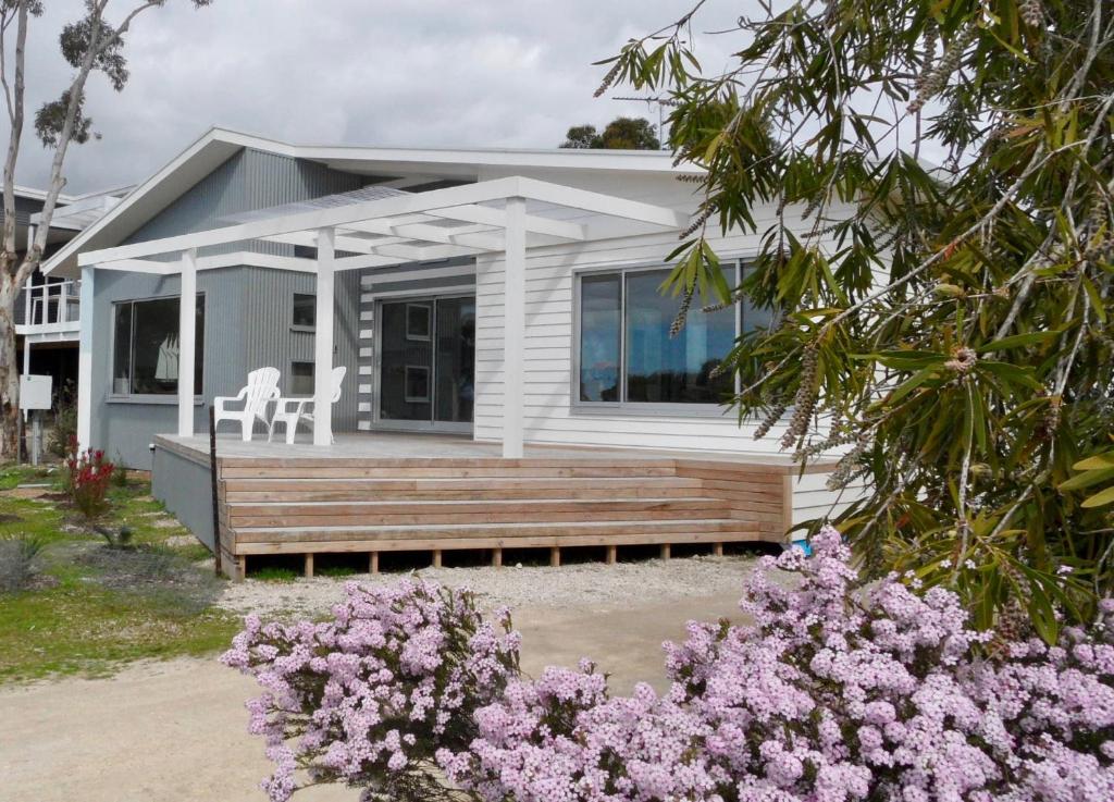 a small white house with a porch and flowers at WHITE SHELLS HOLIDAY RENTAL in Nepean Bay