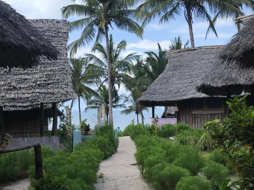 einen Weg zwischen zwei strohgedeckten Häusern mit Palmen in der Unterkunft Mafia Beach Bungalows sea view in Utende