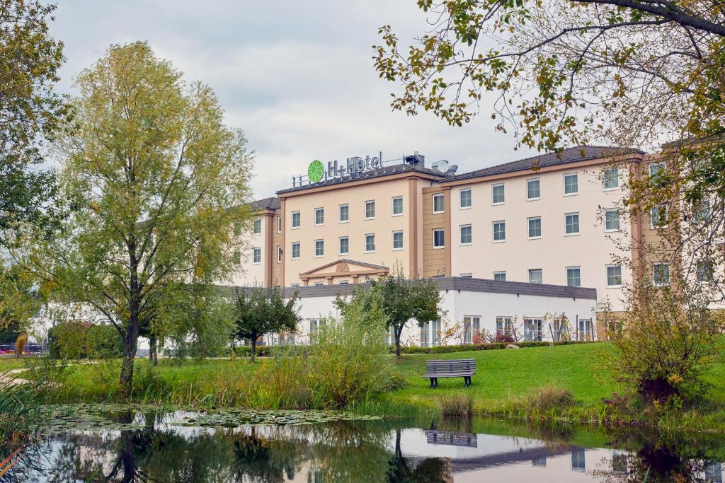 un parc avec un banc, un bâtiment et un étang dans l'établissement H+ Hotel Frankfurt Airport West, à Hofheim am Taunus