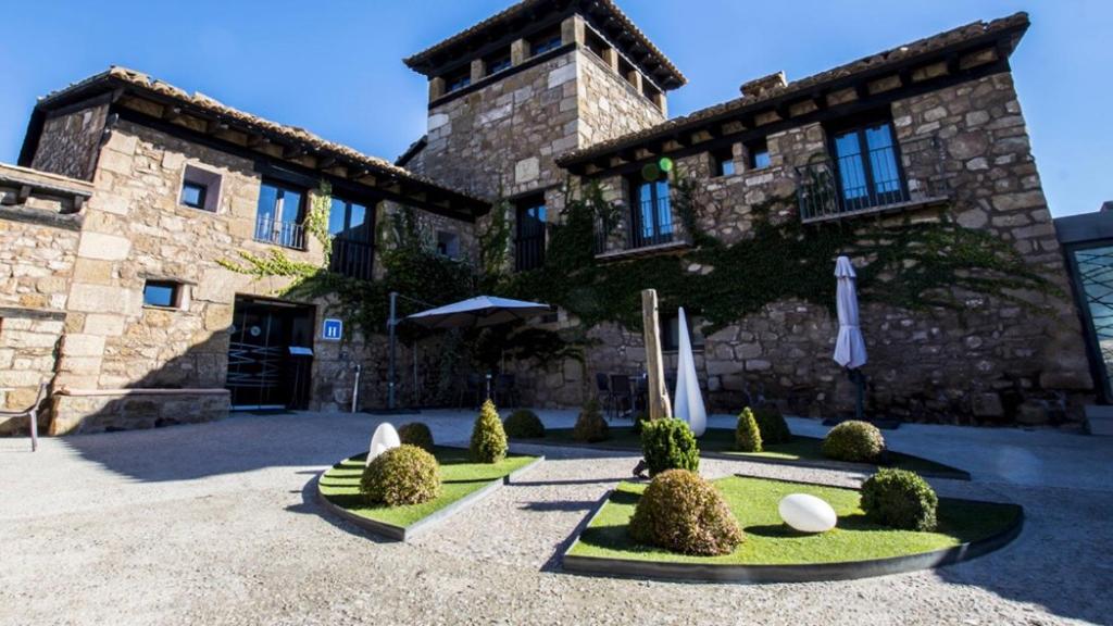 a building with a courtyard with bushes and umbrellas at Hotel Restaurante Masía la Torre in Mora de Rubielos