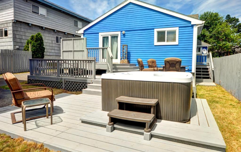 a deck with a hot tub and chairs and a blue house at Pearl off the Prom in Seaside