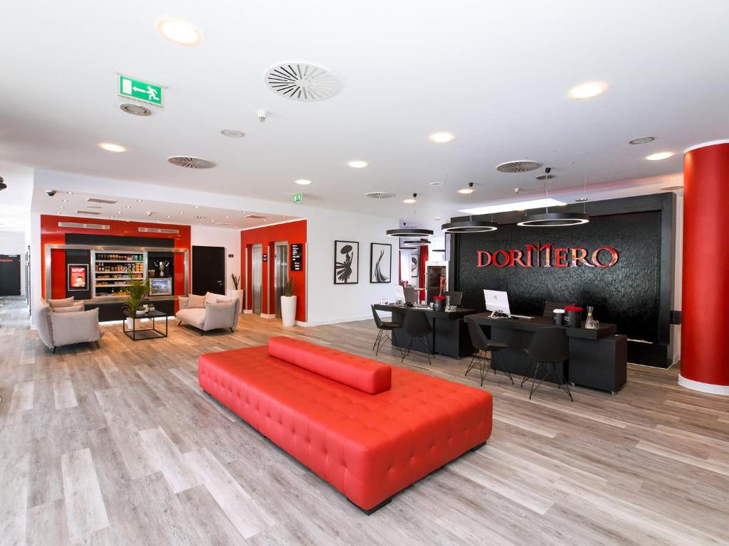 a living room with a red couch and a restaurant at DORMERO Hotel Zürich Airport in Glattbrugg