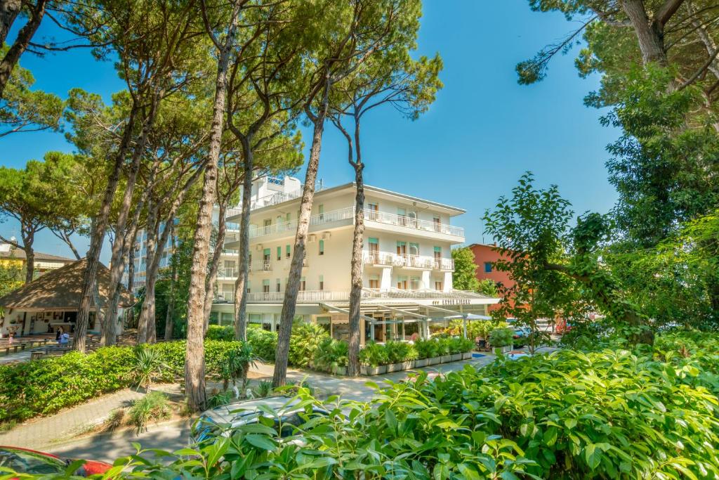 een groot wit gebouw midden tussen de bomen bij Hotel Milano in Eraclea Mare