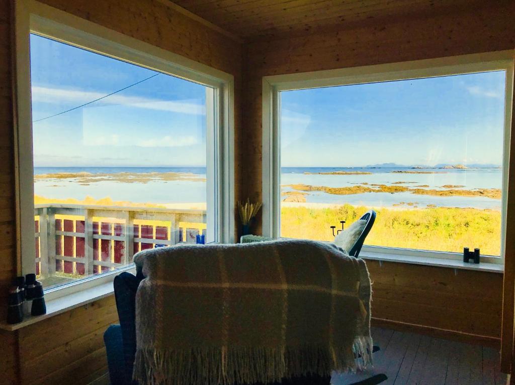 a room with a chair in front of two large windows at Beach View Lofoten in Bøstad