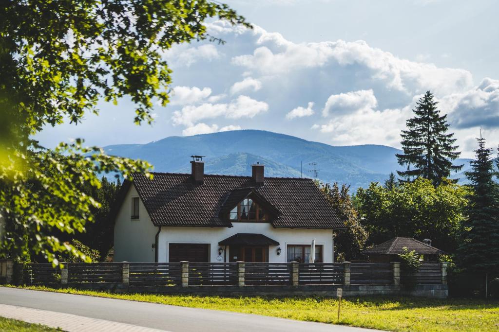 a white house with a fence and mountains in the background at Penzion u lázní in Velké Losiny
