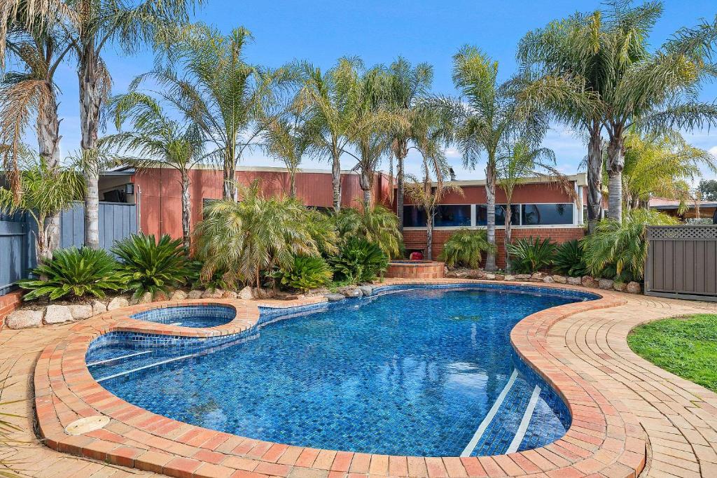 a swimming pool in a yard with palm trees at Peppermill Inn Motel in Shepparton