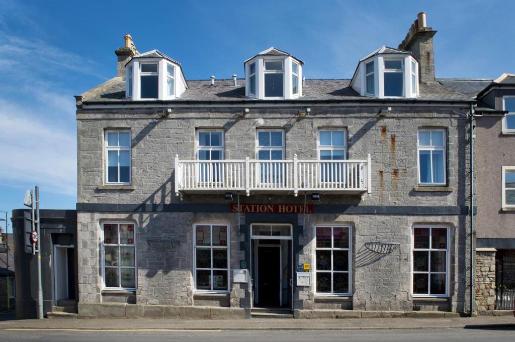 a white building with a blue roof and windows at Station Hotel in Thurso