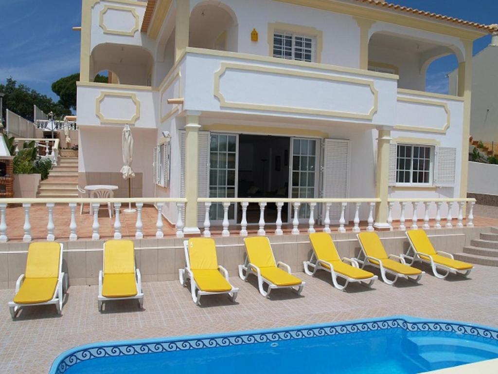 Villa con piscina y tumbonas amarillas. en Apartamento Mariamar en Olhos de Água