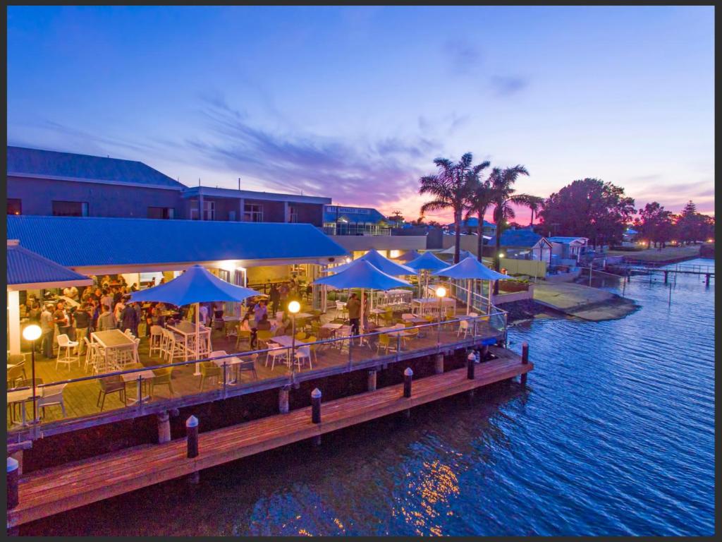 a pier with tables and blue umbrellas on the water at The Parade Hotel in Bunbury