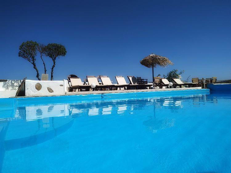 a pool of blue water with chairs and umbrellas at Anatoli Studios in Skhoinoussa