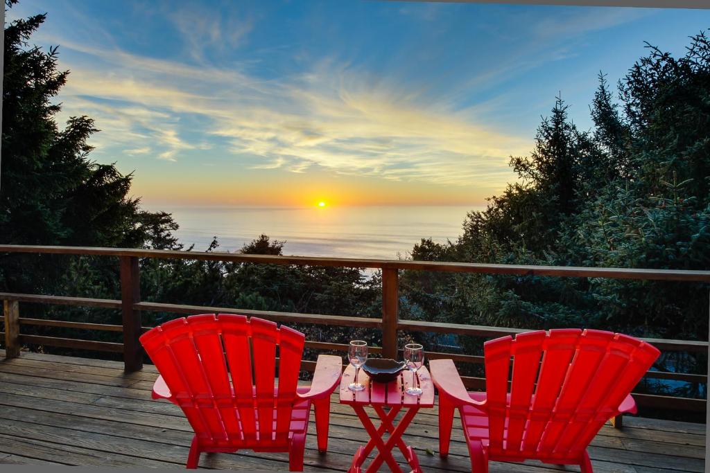 two red chairs and a table on a deck with the sunset at The Anchor House in Lincoln City