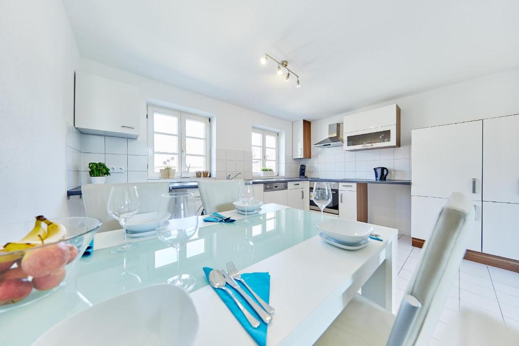 a white kitchen with a large glass table with chairs at Wunderschöne Maisonette-Wohnung für bis zu 10 Personen in Ettenheim