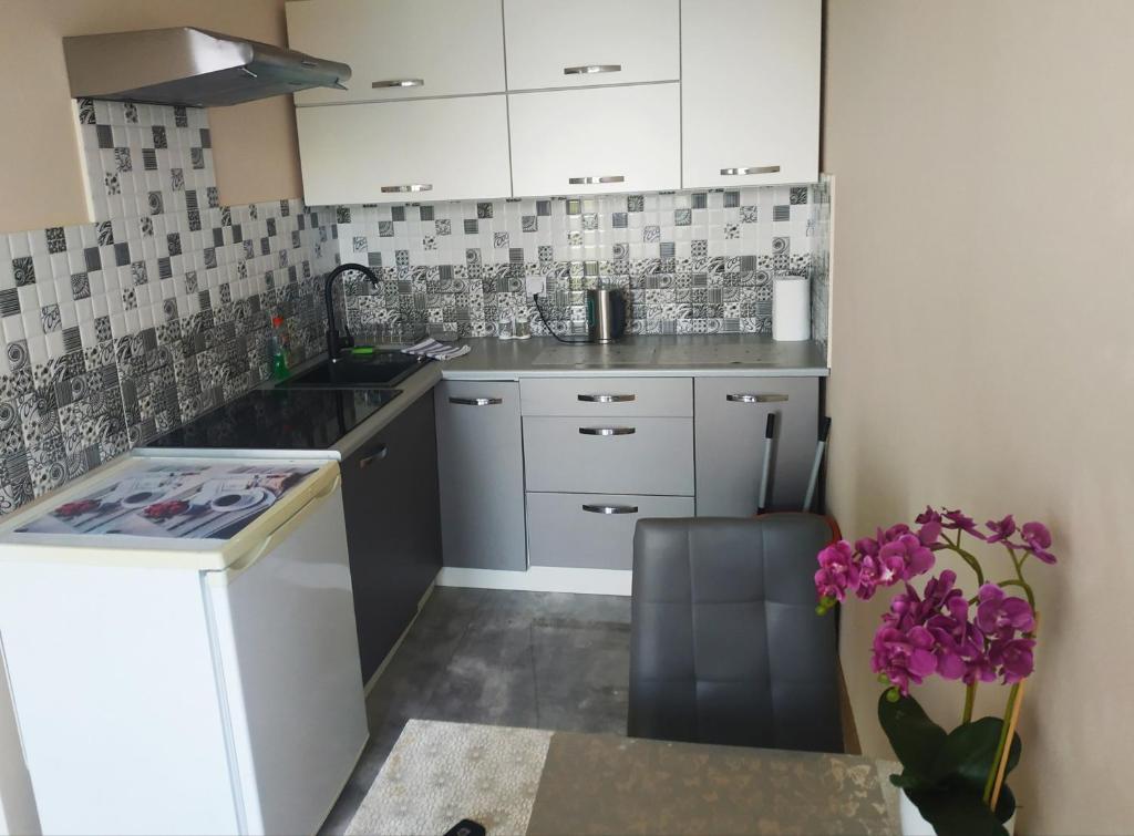 una pequeña cocina con armarios blancos y flores púrpuras en Oskar Apartament Centrum PKP, en Mińsk Mazowiecki