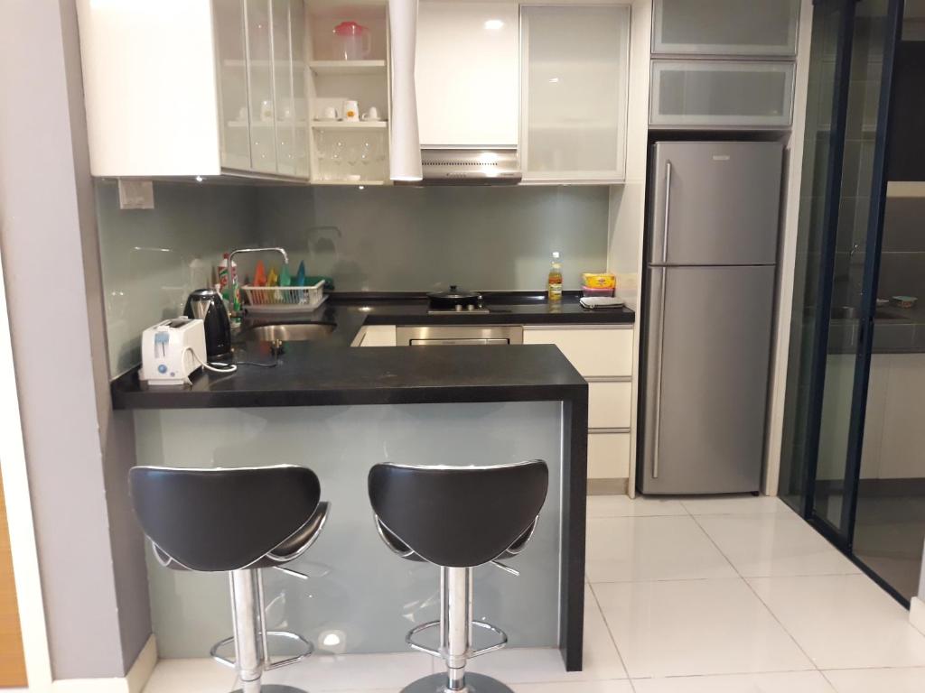 a kitchen with two bar stools and a refrigerator at Comfy Apartment at Casa Residency in Kuala Lumpur