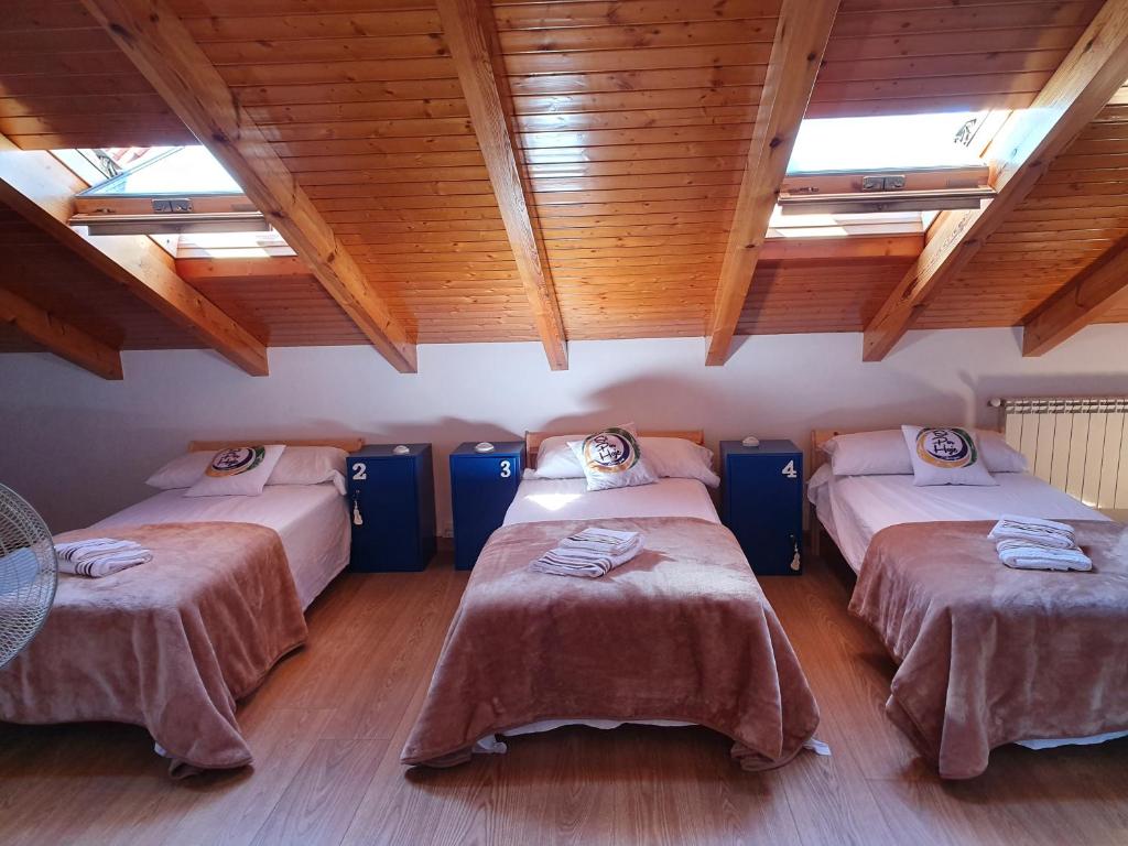 three beds in a room with wooden ceilings at Albergue Só Por Hoje , Albergue de Peregrinos del Caminho de Santiago in Astorga