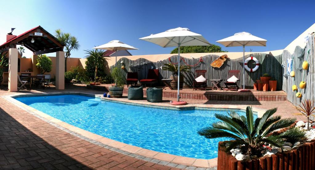 uma piscina com guarda-sóis, mesas e cadeiras em Avenues Guesthouse em Mossel Bay