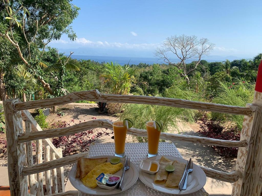 a table with two plates of food and orange juice at La Colina Bungalow in Nusa Penida