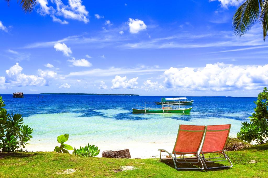 two chairs on a beach with a boat in the water at Retreat Siargao Resort in General Luna