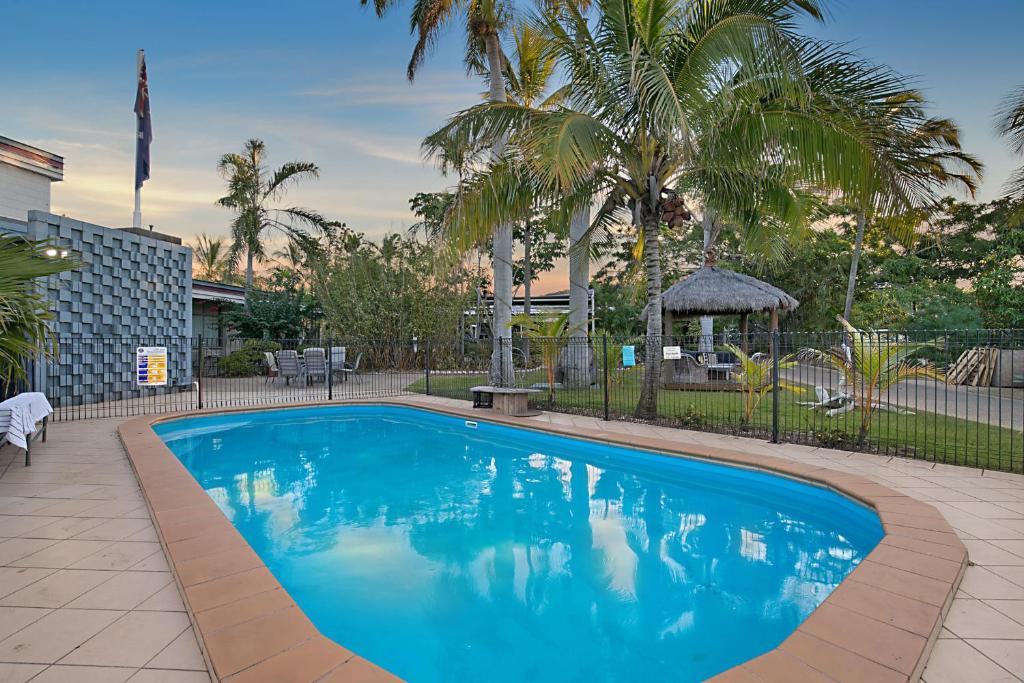 a large blue swimming pool in a yard with palm trees at South Gladstone Motel in Gladstone