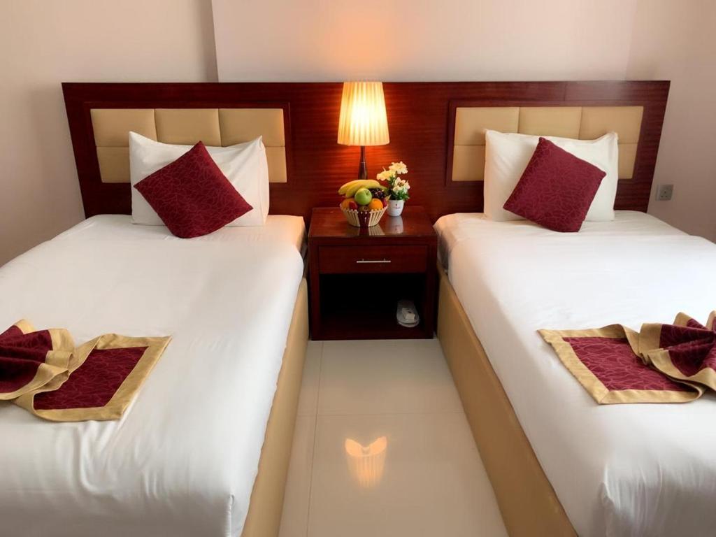 two beds in a hotel room with red pillows at Hala Inn Hotel Apartments - BAITHANS in Ajman 
