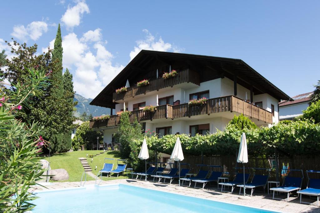 ein Hotel mit Stühlen und Sonnenschirmen neben einem Pool in der Unterkunft Pension Sankt Urban in Meran
