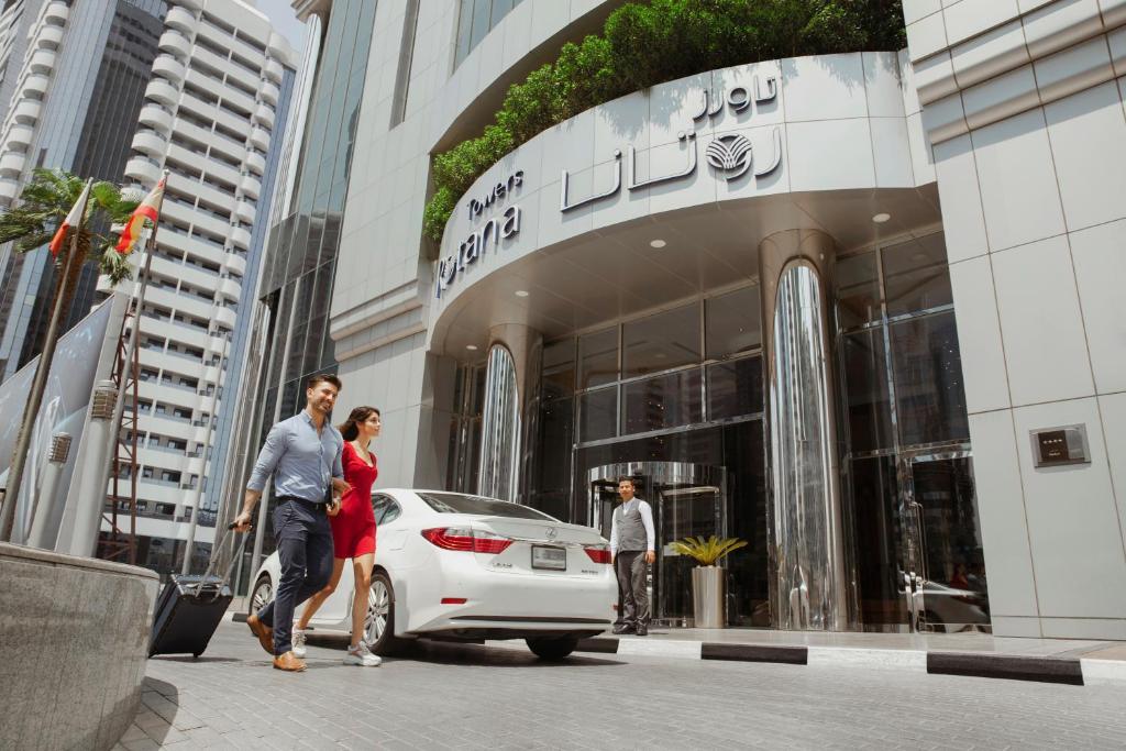 杜拜的住宿－迪拜羅塔納大廈酒店，男人和女人在大楼前走过一辆白色汽车