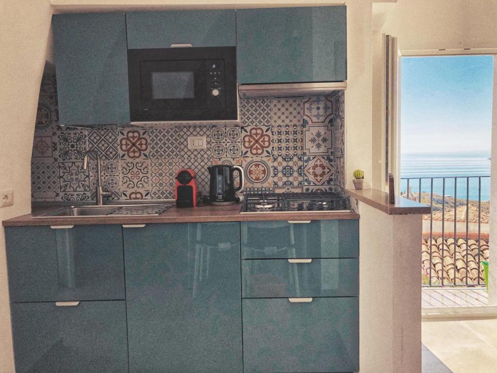 uma cozinha com armários azuis e vista para o oceano em Fico d’India apartments em Monte SantʼAngelo