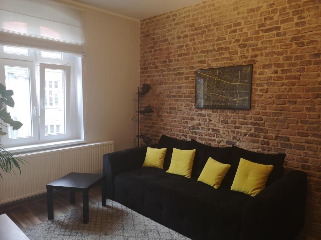 カトヴィツェにあるIndustrialny apartament Mariackaのリビングルーム(黒いソファ、黄色い枕付)