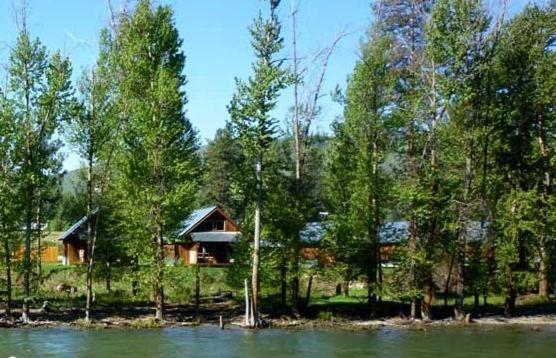 a house on the shore of a lake with trees at Methow River Lodge Cabins in Winthrop