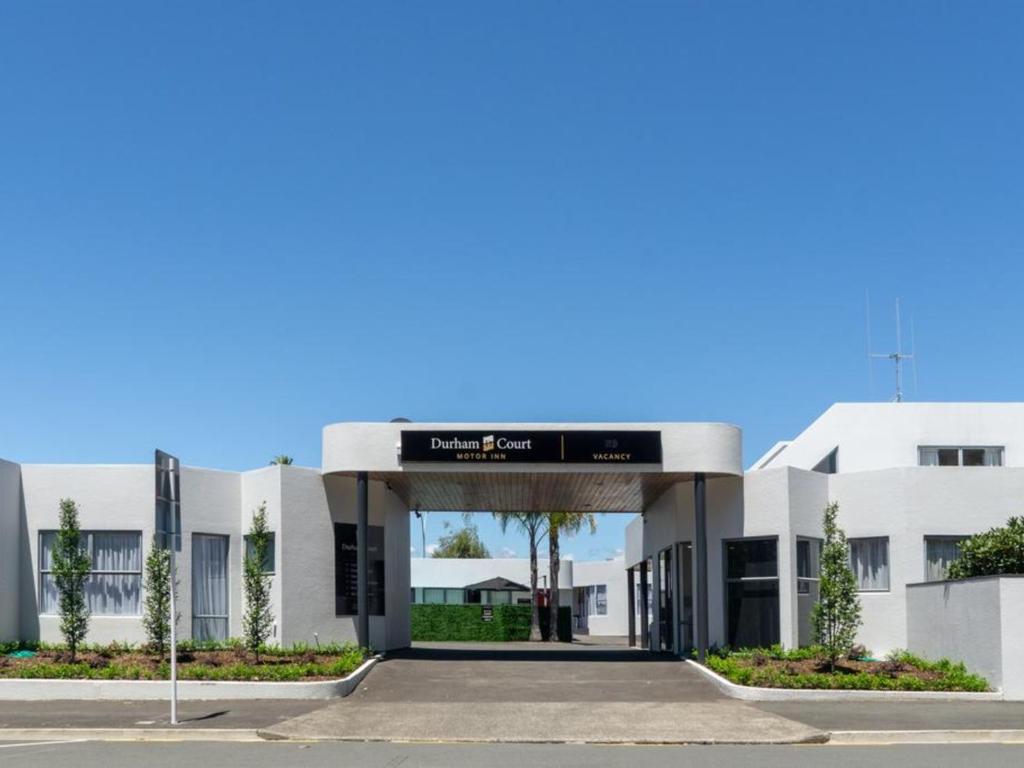 un gran edificio blanco con un cartel. en Durham Court Motor Inn, en Tauranga