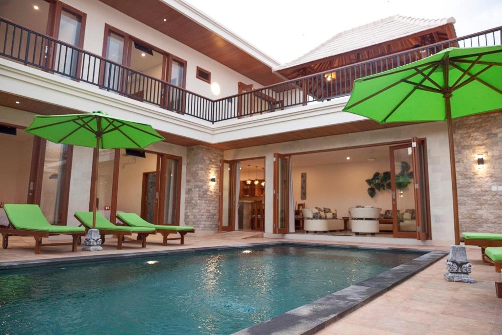 a swimming pool with green chairs and umbrellas at Pineapple Villa Sanur in Sanur