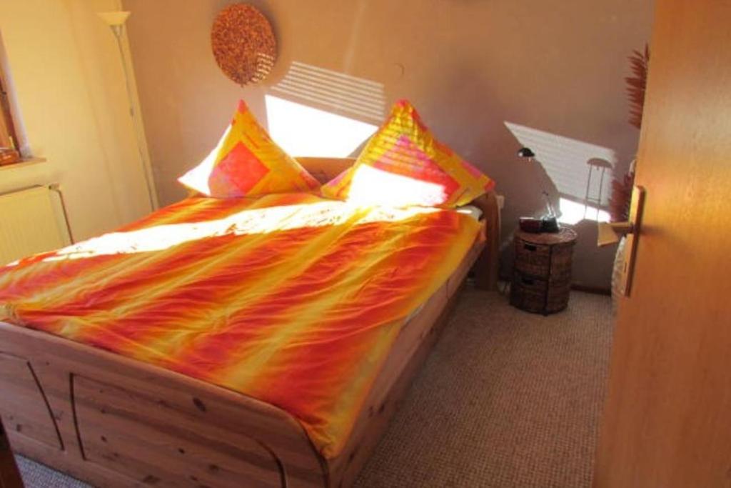 a bed with an orange comforter and colorful pillows at Gemütliche Ferienwohnung in ländlicher Idylle in Vöhl