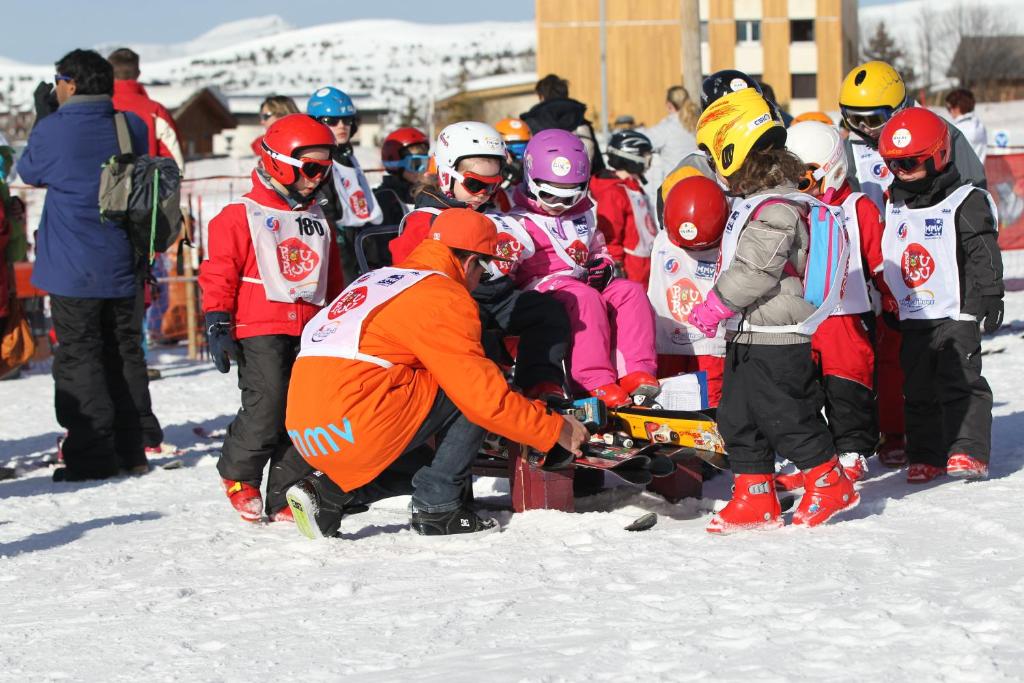 a group of children standing around a man in the snow at Hôtel Club mmv Les Bergers **** in L'Alpe-d'Huez