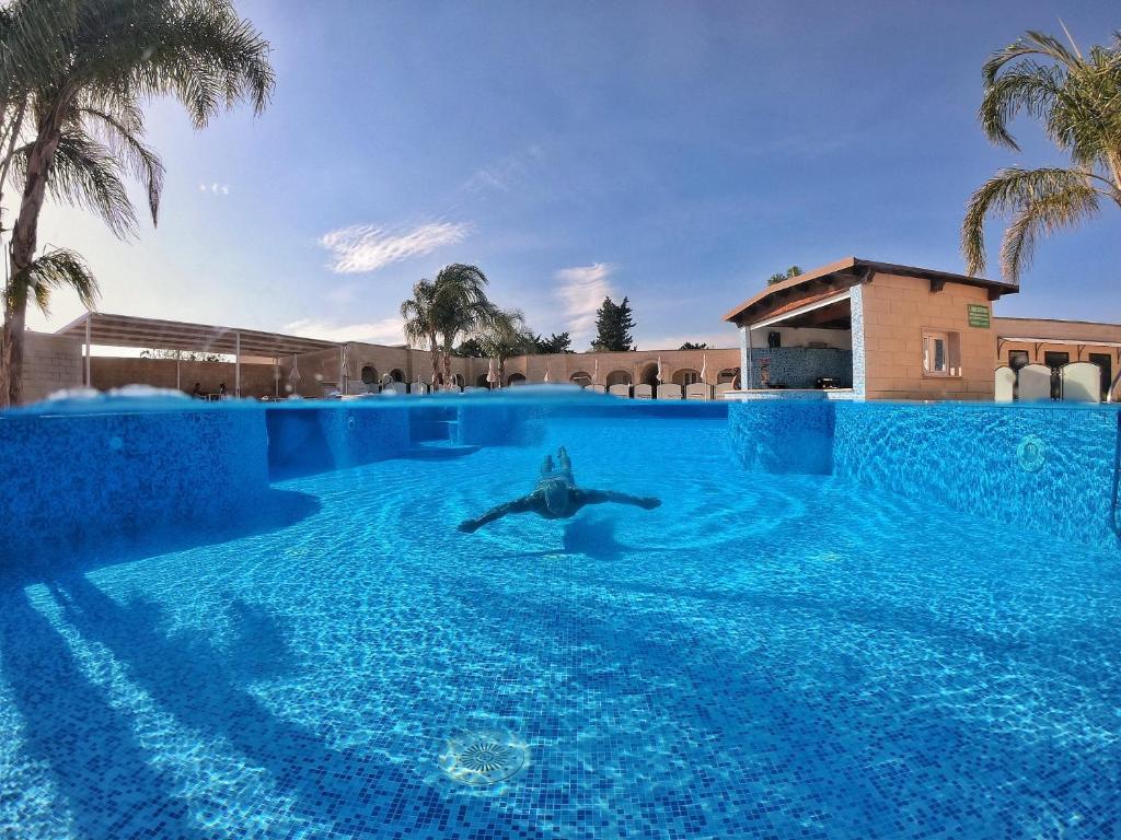 a person swimming in a large pool with palm trees at La Pineta Residence in Otranto