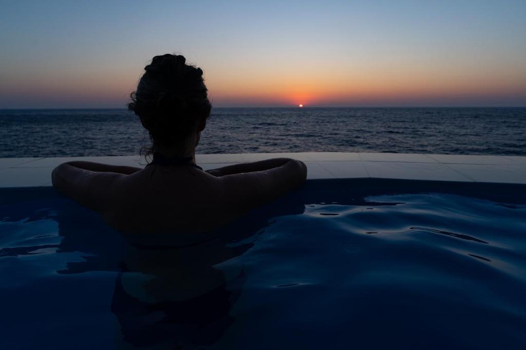 a man sitting in a swimming pool watching the sunset at Ikarian Endless Blue in Kouniádhoi
