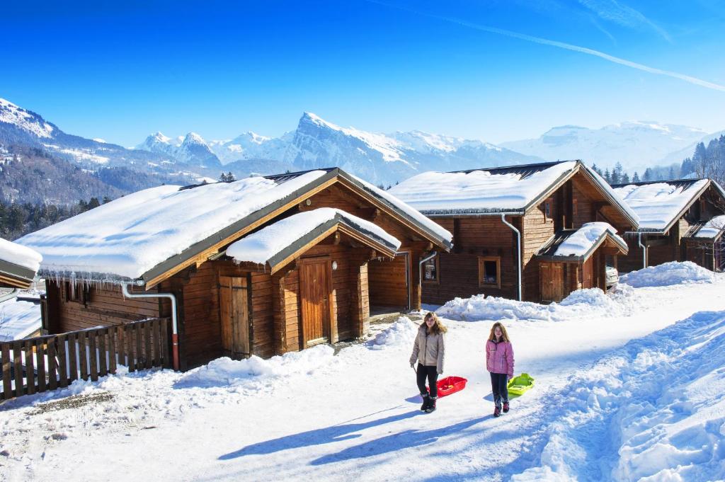 Deux filles marchant dans la neige près d'une cabine dans l'établissement Résidence Néméa Les Chalets du Bois de Champelle, à Morillon