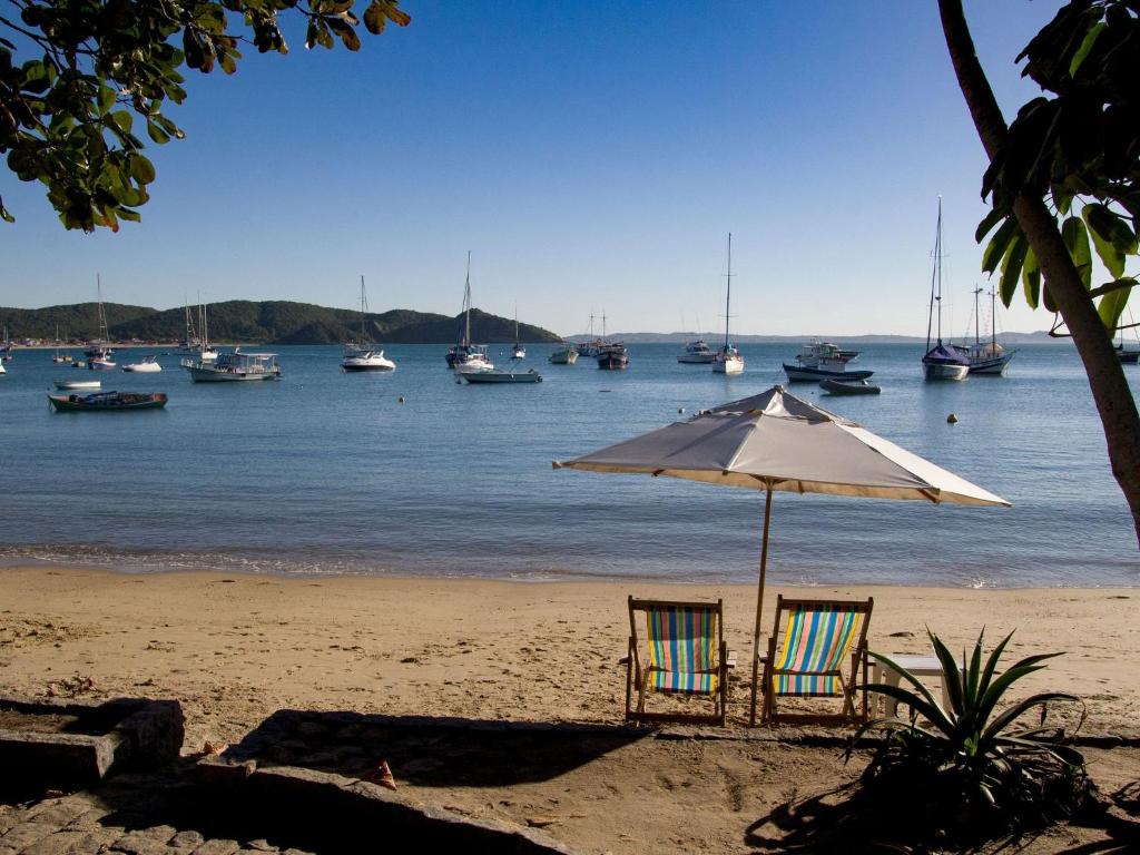 um guarda-sol e cadeiras numa praia com barcos na água em Mansão com Seis Suítes Pé na Areia da Praia dos Ossos e Próx. à Rua das Pedras Por Luxury Rentals em Búzios