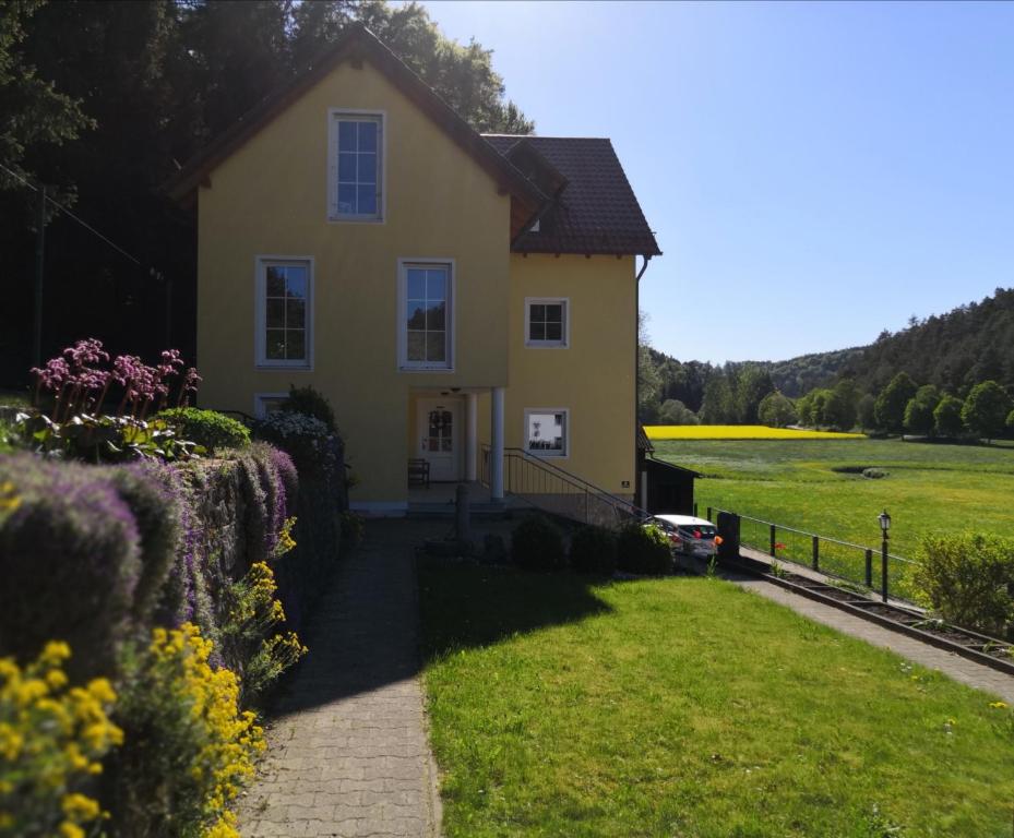 een geel huis met een gazon en bloemen bij Ferienhaus am Bach in Deuerling