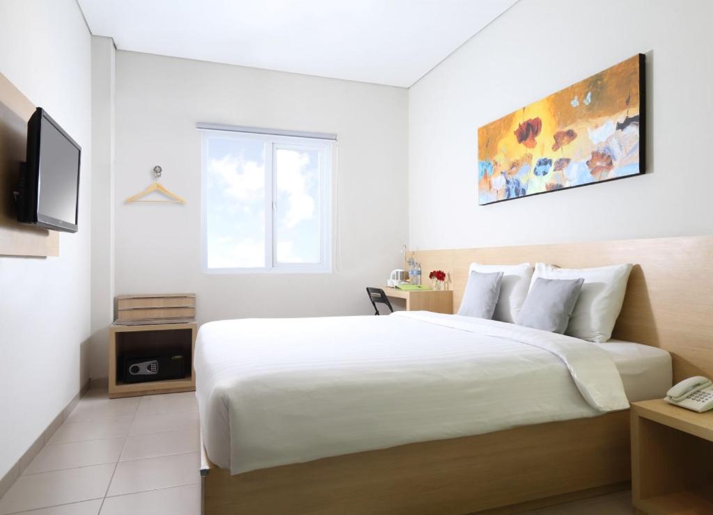 a white bedroom with a large bed and a television at Lemo Hotel Serpong in Serpong