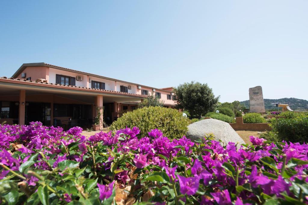 un jardin avec des fleurs violettes en face d'un bâtiment dans l'établissement Hotel Su Giudeu, à Chia