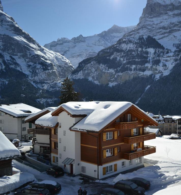 a building covered in snow with mountains in the background at Hotel Caprice - Grindelwald in Grindelwald