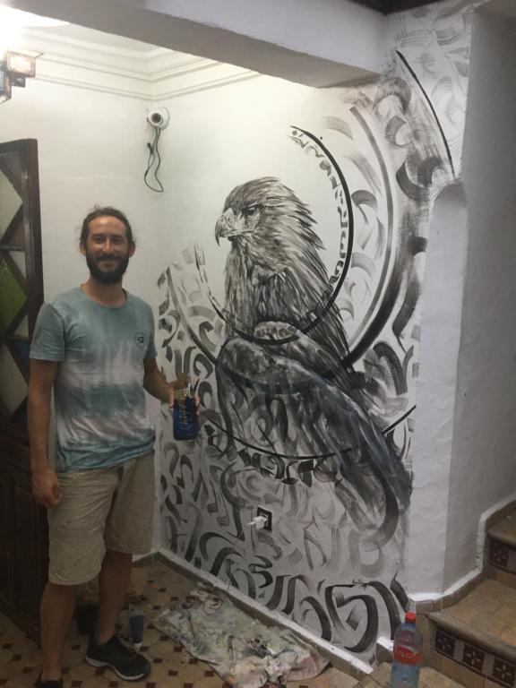 un hombre de pie junto a una pintura de un pájaro en una pared en The Medina Hostel, en Tánger